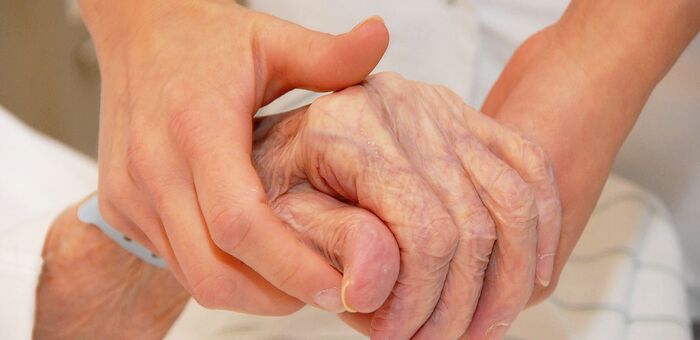 Alte Patientin reicht Pflegerin die Hand